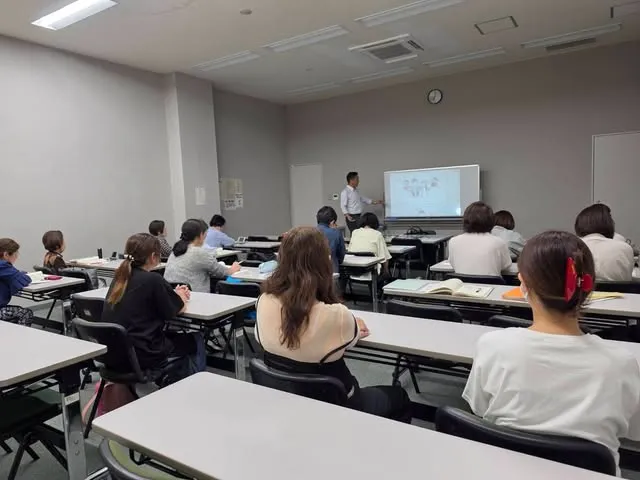 教室で、ホワイトボードの前の講師の話を聞く参加者のみなさん